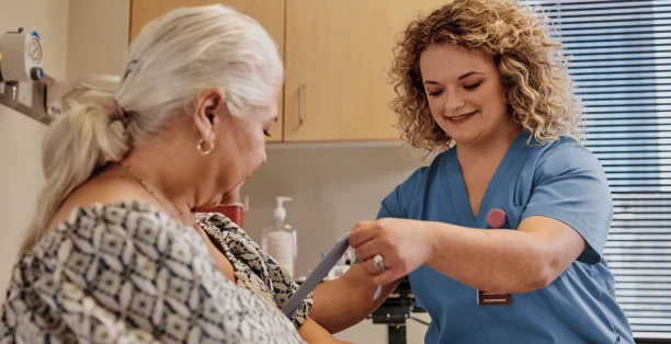 Female phlebotomist in blue scrubs tying rubber band around patient's arm