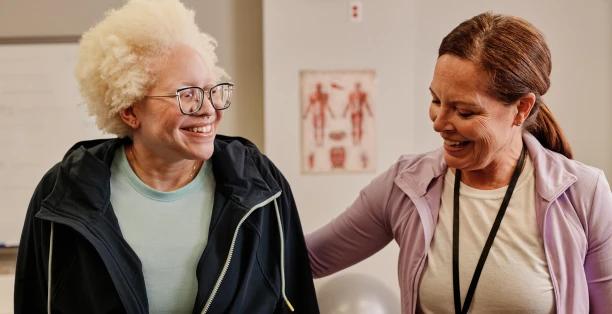 Female healthcare worker in purple jacket smiling at elderly female patient