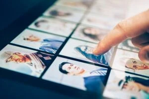 Finger pointing to woman within grid of phonos on tablet screen