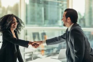 Black businesswoman shakes hand with businessman across table desk in modern business office well-dressed after agreement partnership job interview