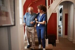 Mature female nurse walking with senior man on steps at home