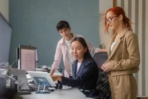 Three office workers collaborating at a desk looking at information on a screen.