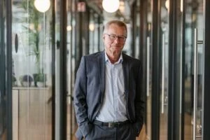 Mature businessman standing in a corridor in his office building, wearing a suit with his hands in his pockets.