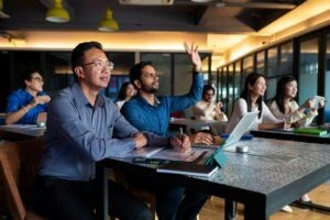 Group of colleagues sitting in training room, with one raising hand for question