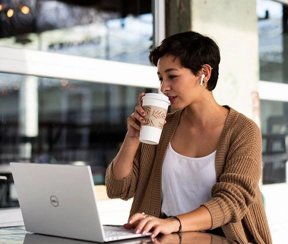 Woman with a coffee working with a laptop and headphones at a cafe table