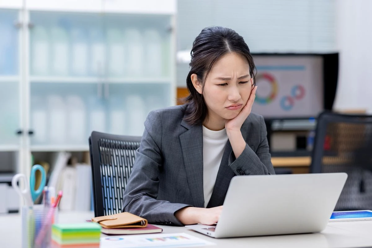 デスクでPCを見ながら顔をしかめる女性