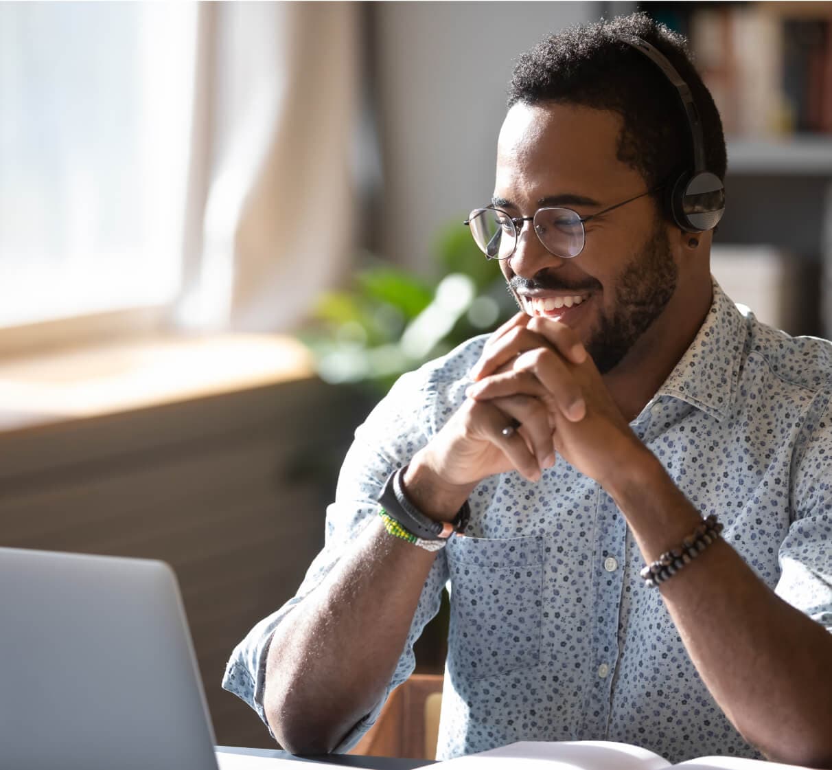 眼鏡とヘッドホンを持った男性が居間に快適に座り、コンピューターの画面を見ながら大きく笑っている。