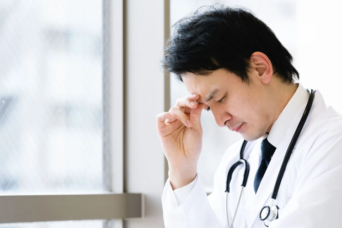 額を指で押さえている医師