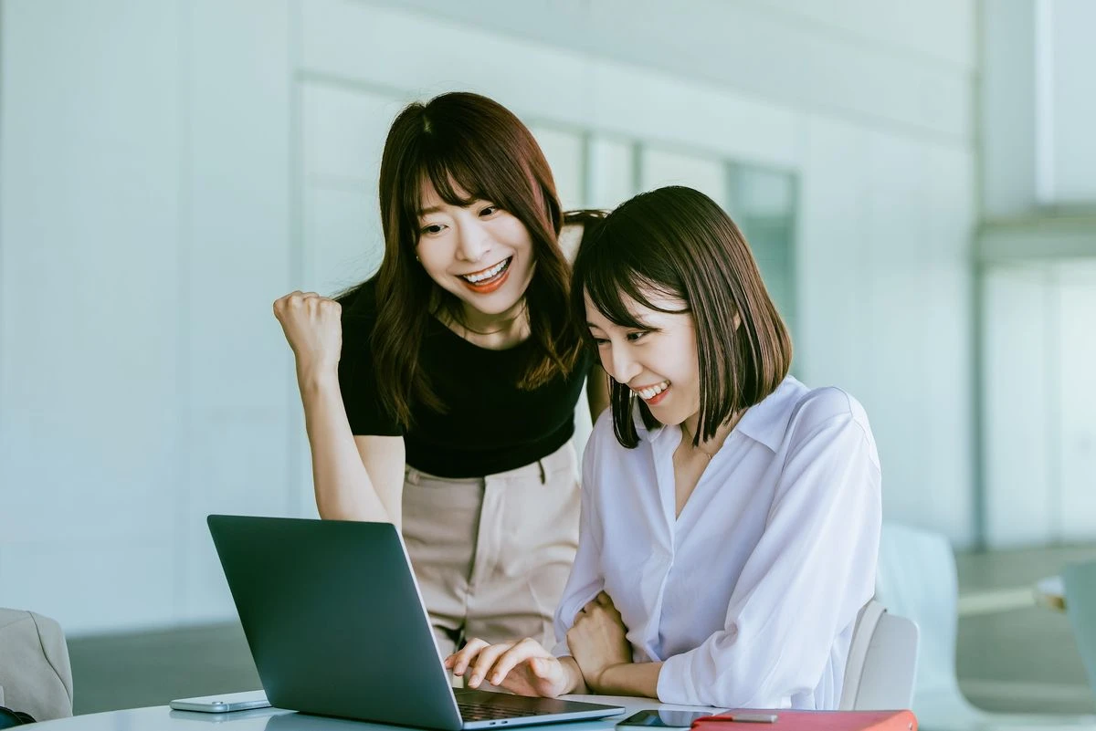 Two women in an office looking at a laptop and smilling