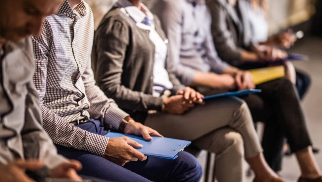 Image is a close up of a row of people dressed in business attire. They appear to be in a conference or large meeting.