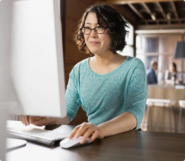 Woman wearing a green shirt sitting at a computer desk using a mouse and keyboard