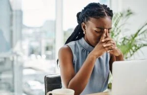 Stressed woman sitting at her desk with her hands rubbing her face