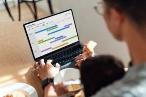 Una mujer, sentada en casa, con un bebé en su regazo, escribiendo en su laptop.