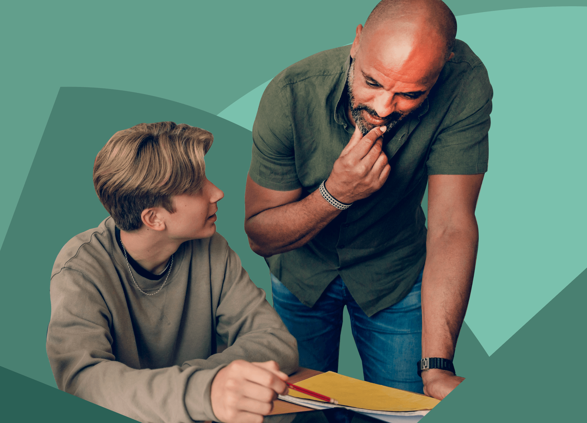 Male teacher leaning on desk, helping teen male student