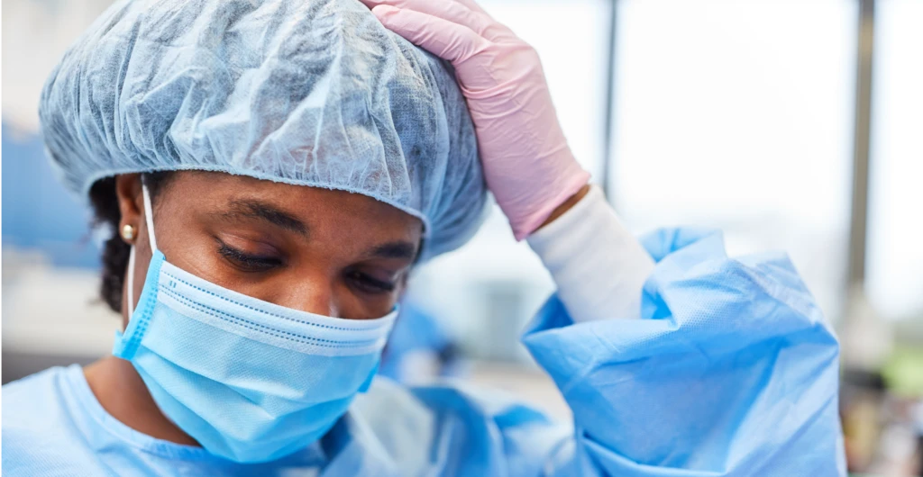 Female nurse in scrubs with left hand on head looking burned out
