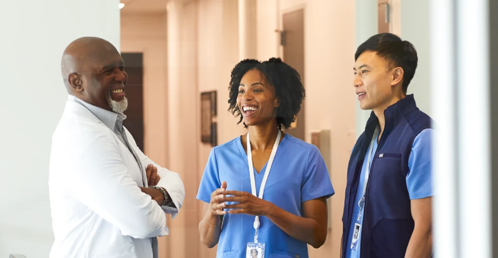 One male doctor smiling and speaking with a female and male nurse