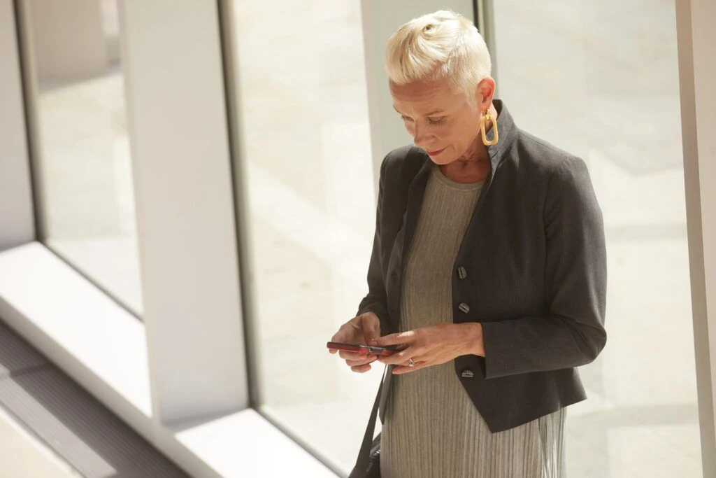 An older business woman types something on her phone.