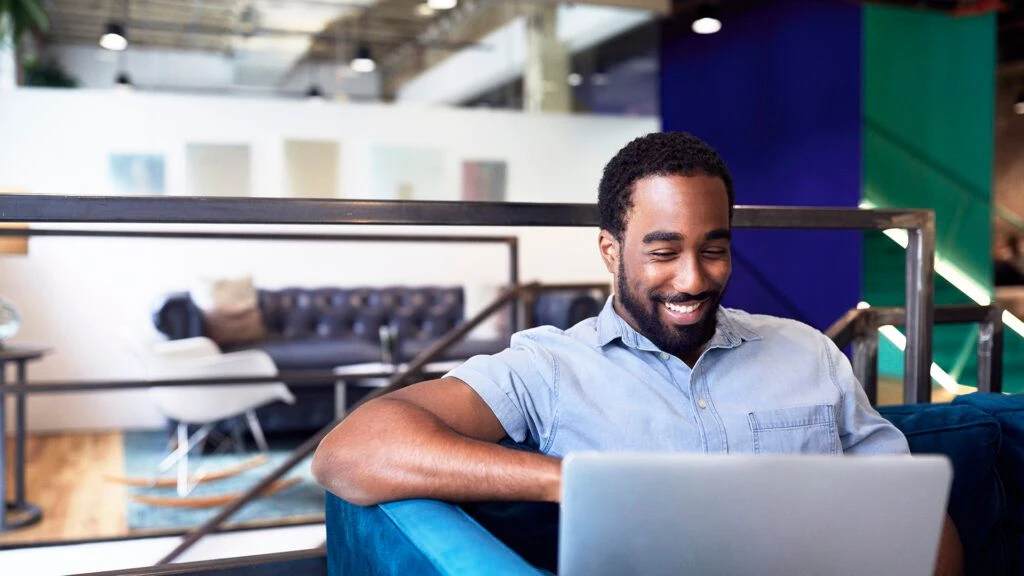 Smiling young businessman using laptop while sitting on sofa at office