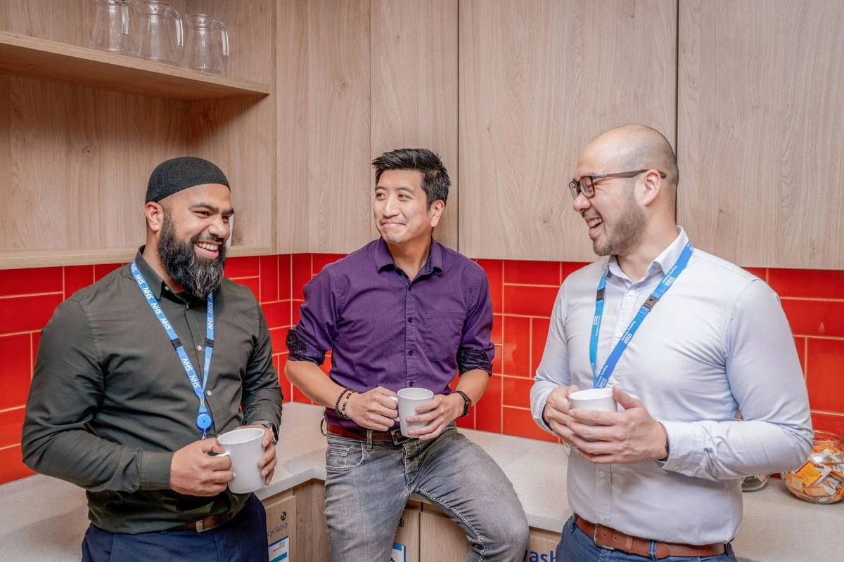 Three professionals chat in a workplace kitchen