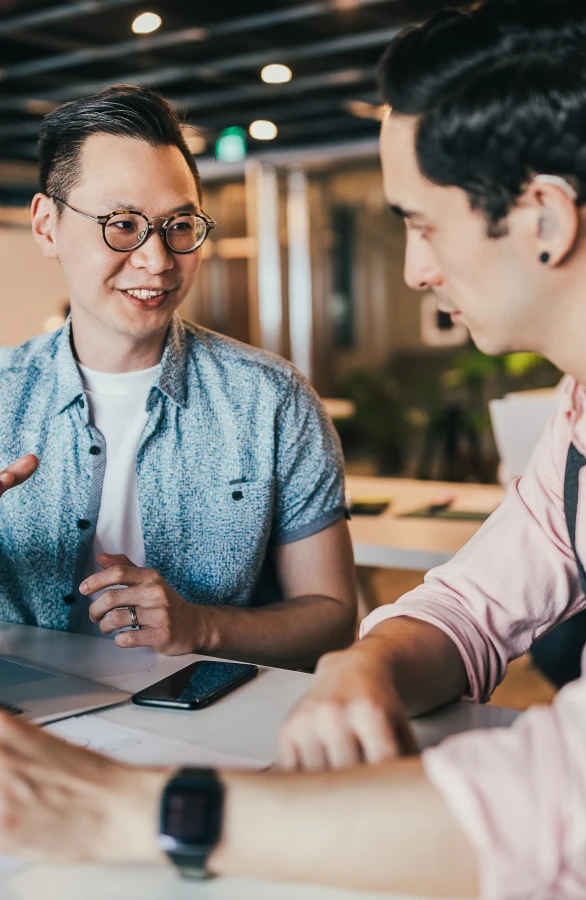 Two men at talking at work in an open office environment