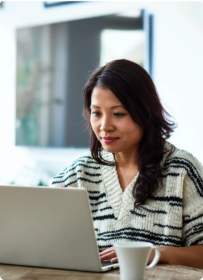 Woman at a table working on her laptop with a coffee cup in the foreground. 