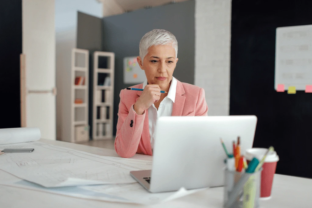 Eine Frau mit einem Stift in der Hand, die nachdenklich auf ihren Laptop blickt