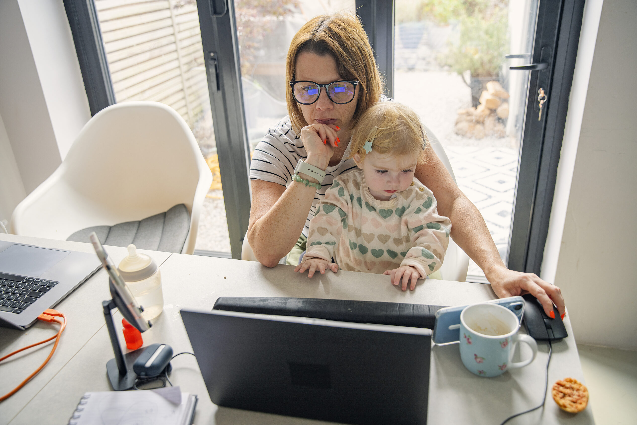 Working parent looking at computer with toddler on their lap
