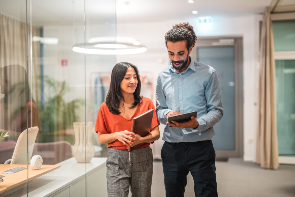 Two colleagues walking down a hallway in the office looking at their tablets