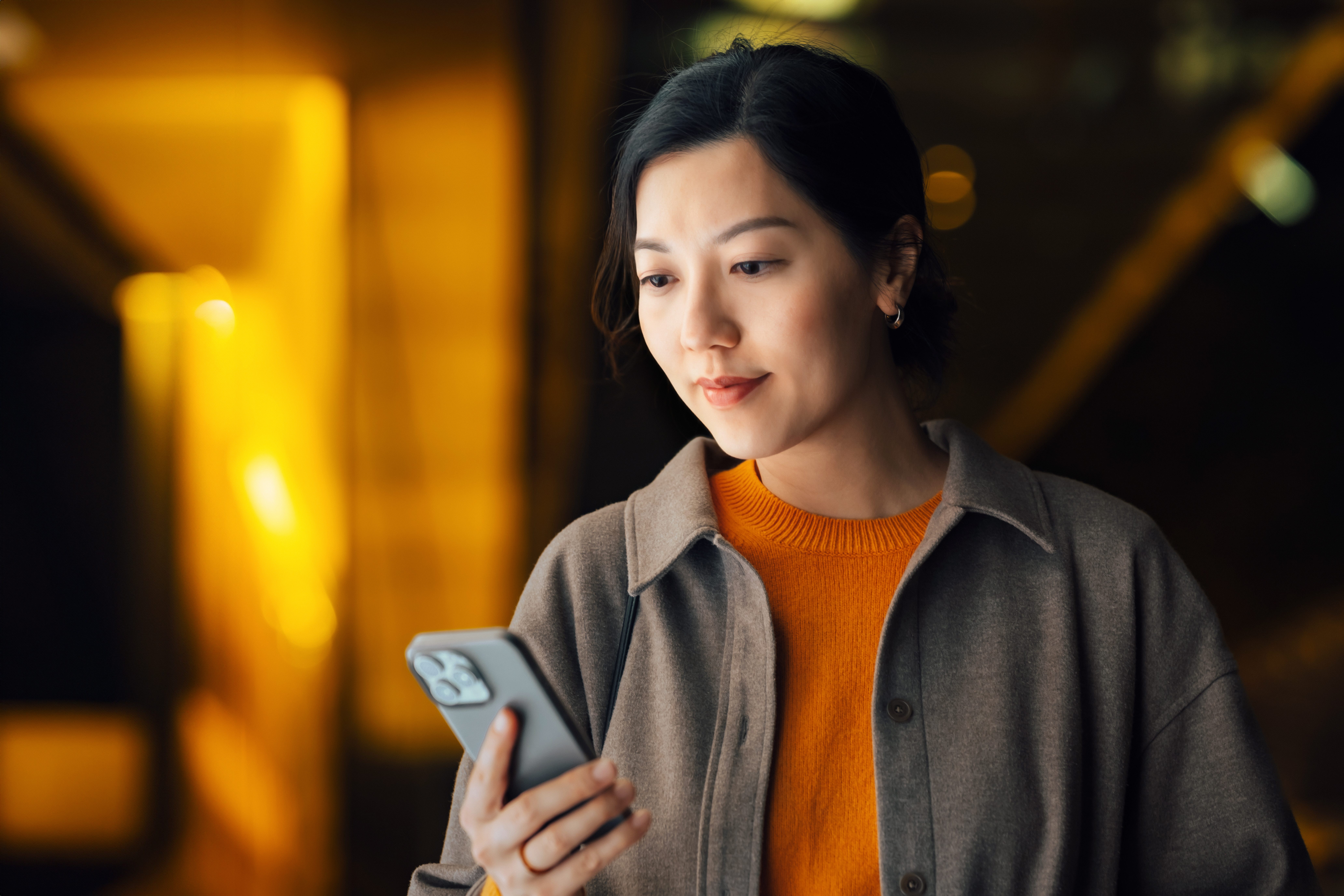 Young person using her smartphone to stay connected while commuting in the city at night. Defocused and illuminated city street lights in background.