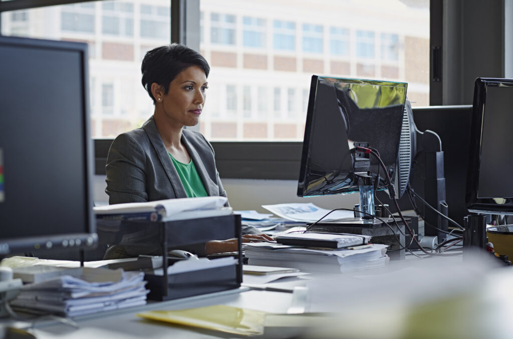 Person using desktop pc in the office with windows behind and papers on desk
