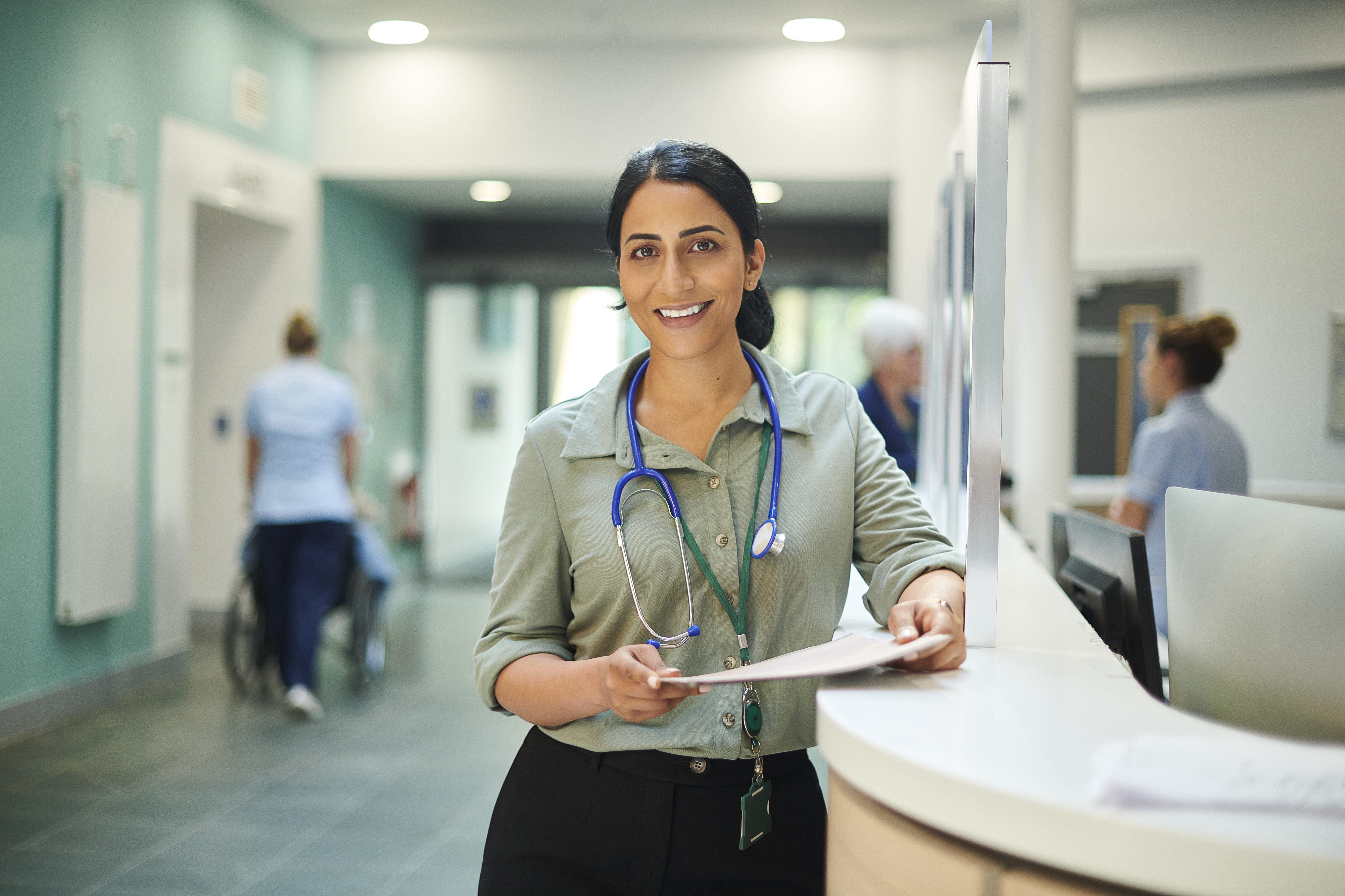 A smiling healthcare consultant holds a chart in the lobby of a hospital