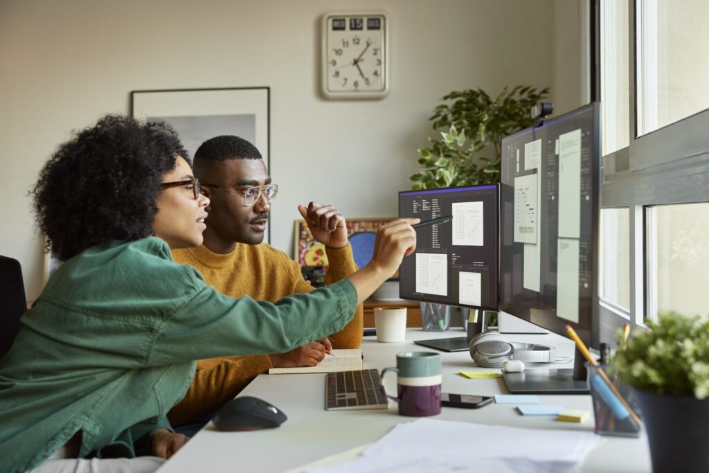 Two people collaborating at desk with multiple screens