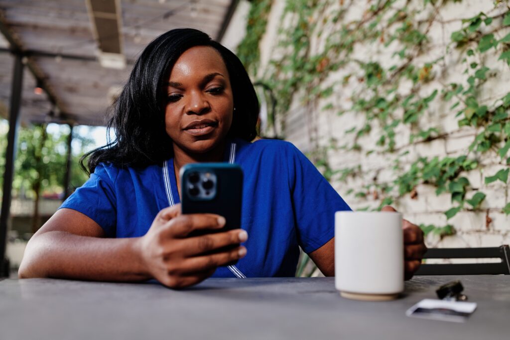 Healthcare worker using mobile phone and drinking coffee while sitting on break