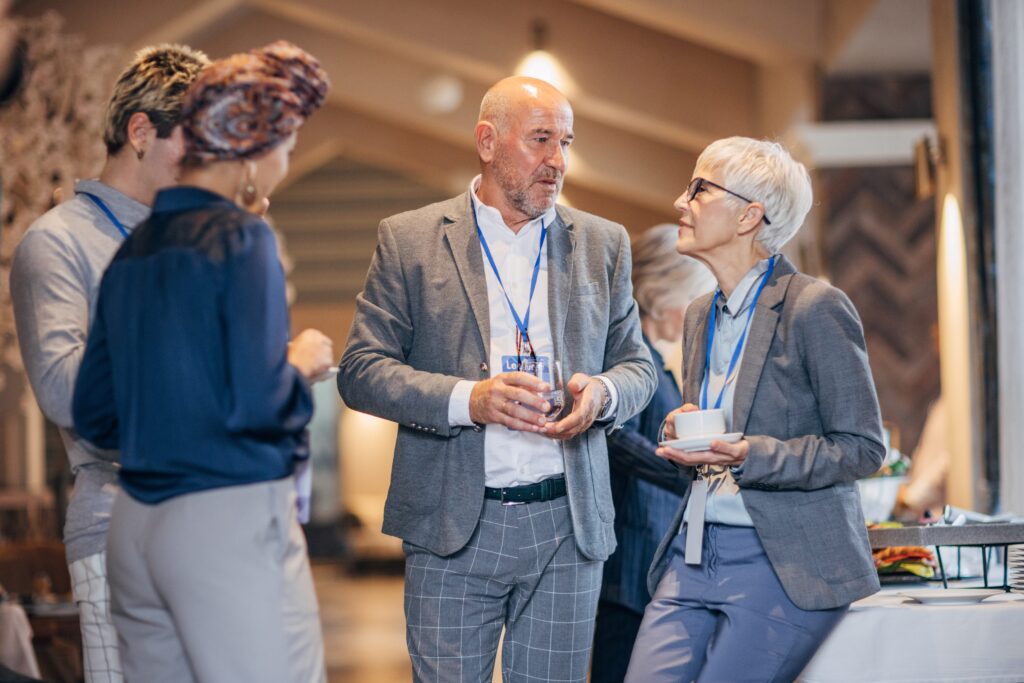 Colleagues networking during a corporate event. They are wearing suits and nametags and seem to be in a convention center.