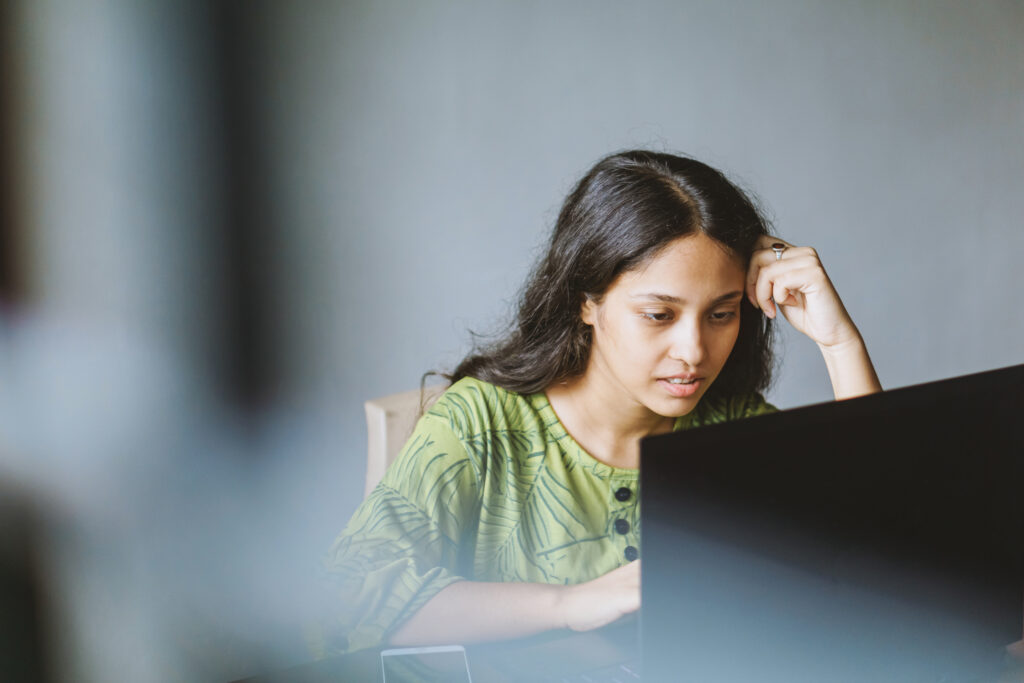 Shot of a Young person using a smartphone and laptop in her workspace through the window.