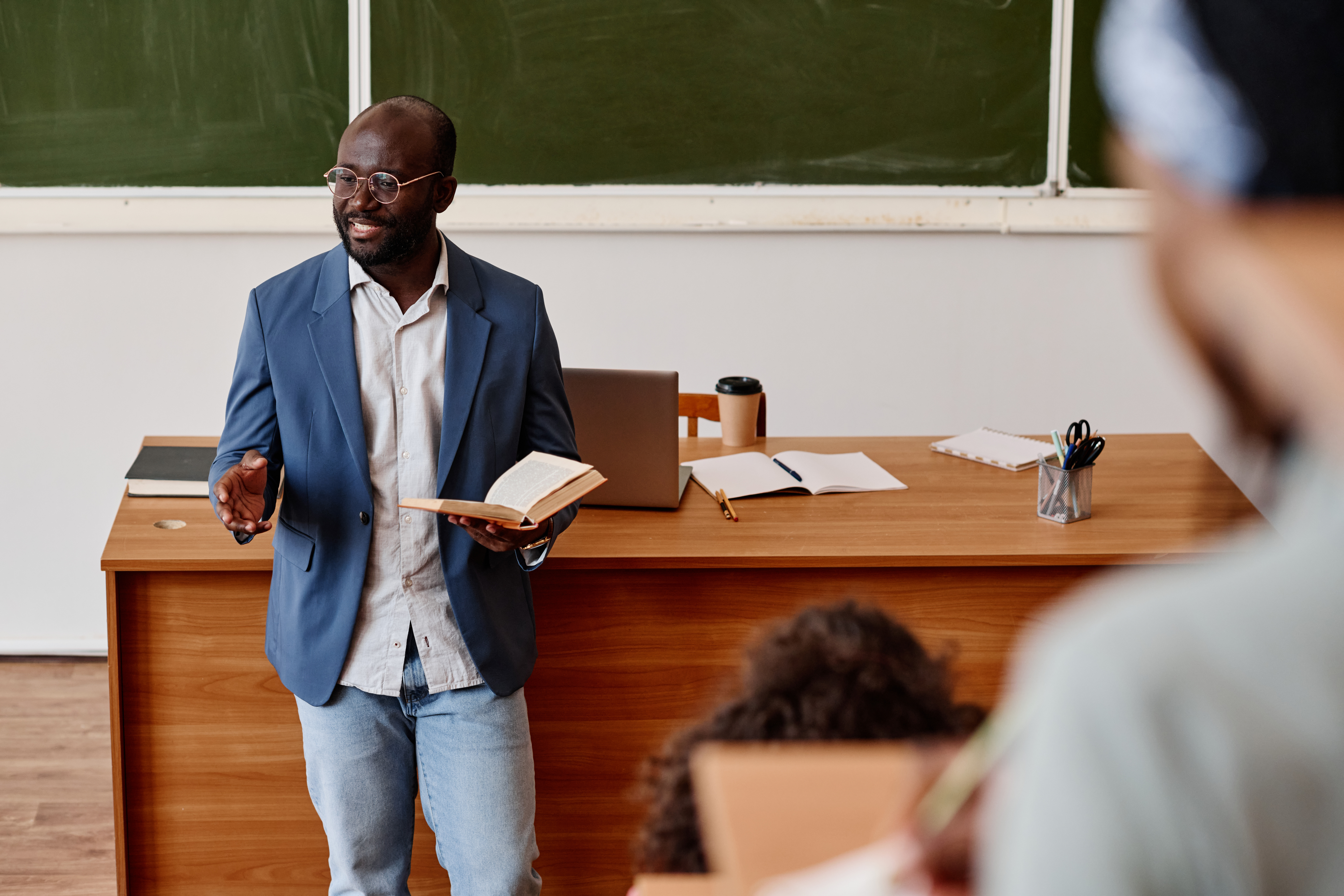 Professor standing in front of class reading lecture from book in hand