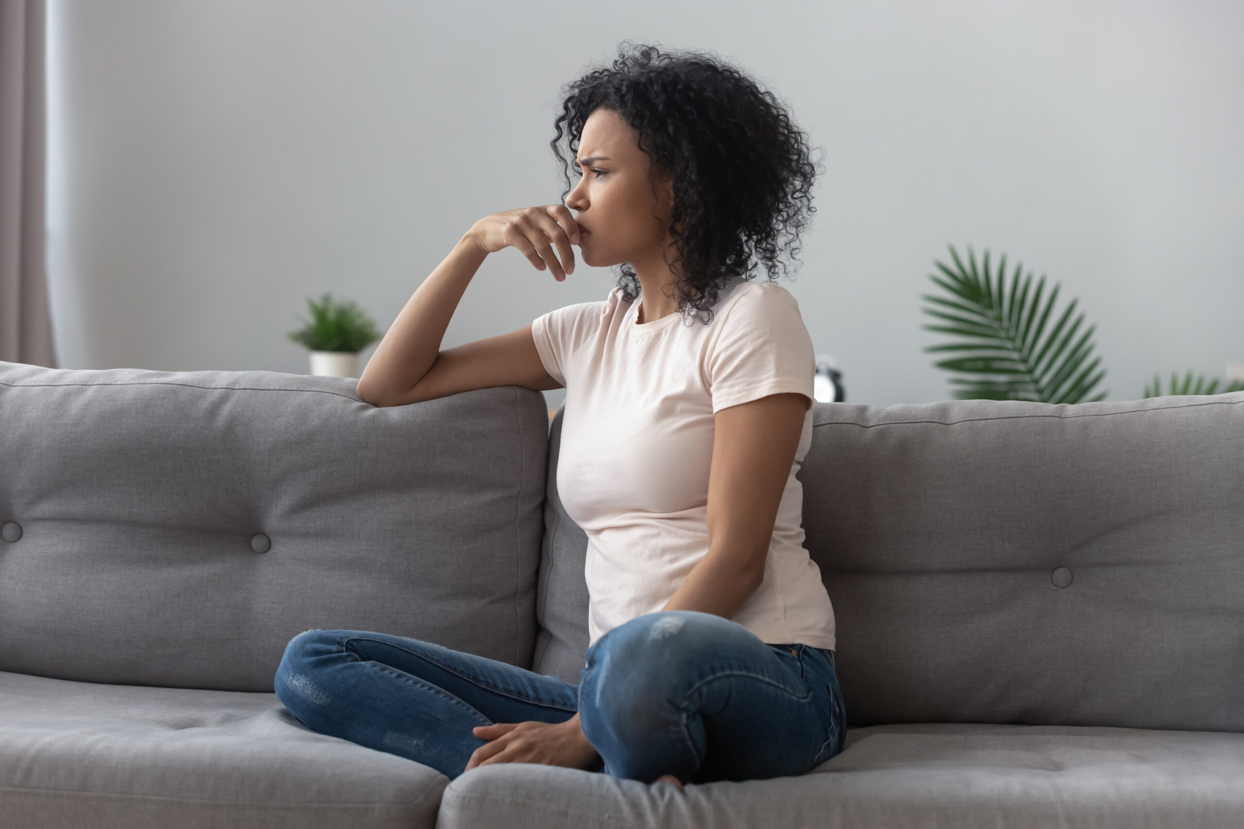 Pensive person sitting on couch in living room looking worried