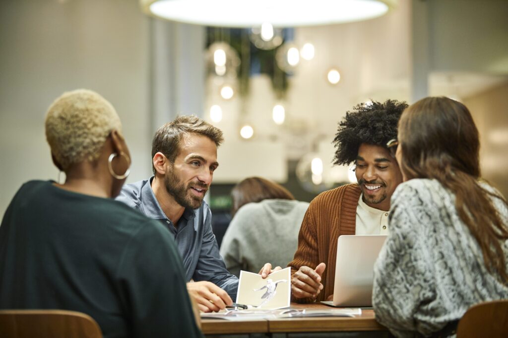 Coworkers gathered for a meeting around a round table in the office. They are smiling.