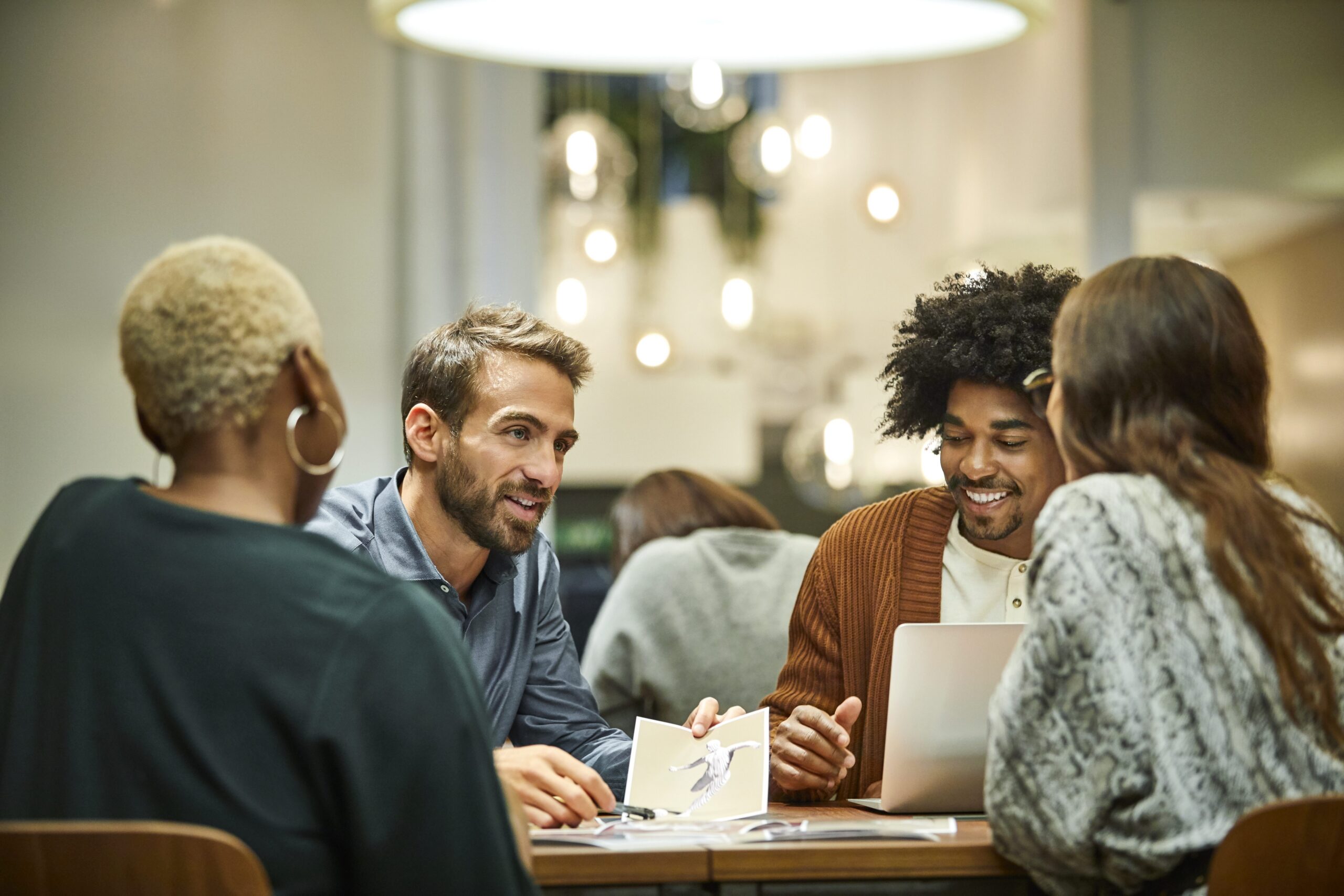Coworkers gathered for a meeting around a round table in the office. They are smiling.