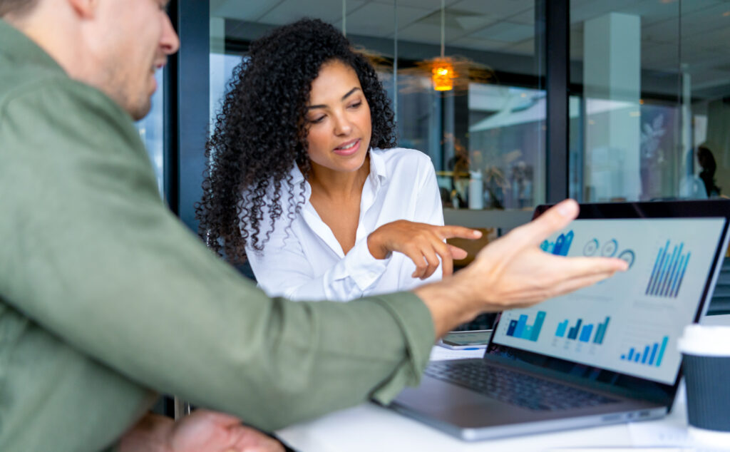 Two people meeting in the office with one person showing another data on a computer with graphs and charts