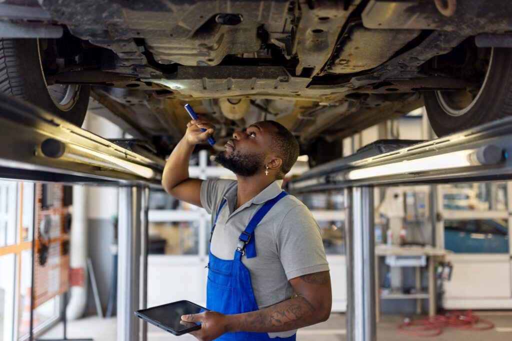 Mechanic using a flashlight to look at the underside of a car