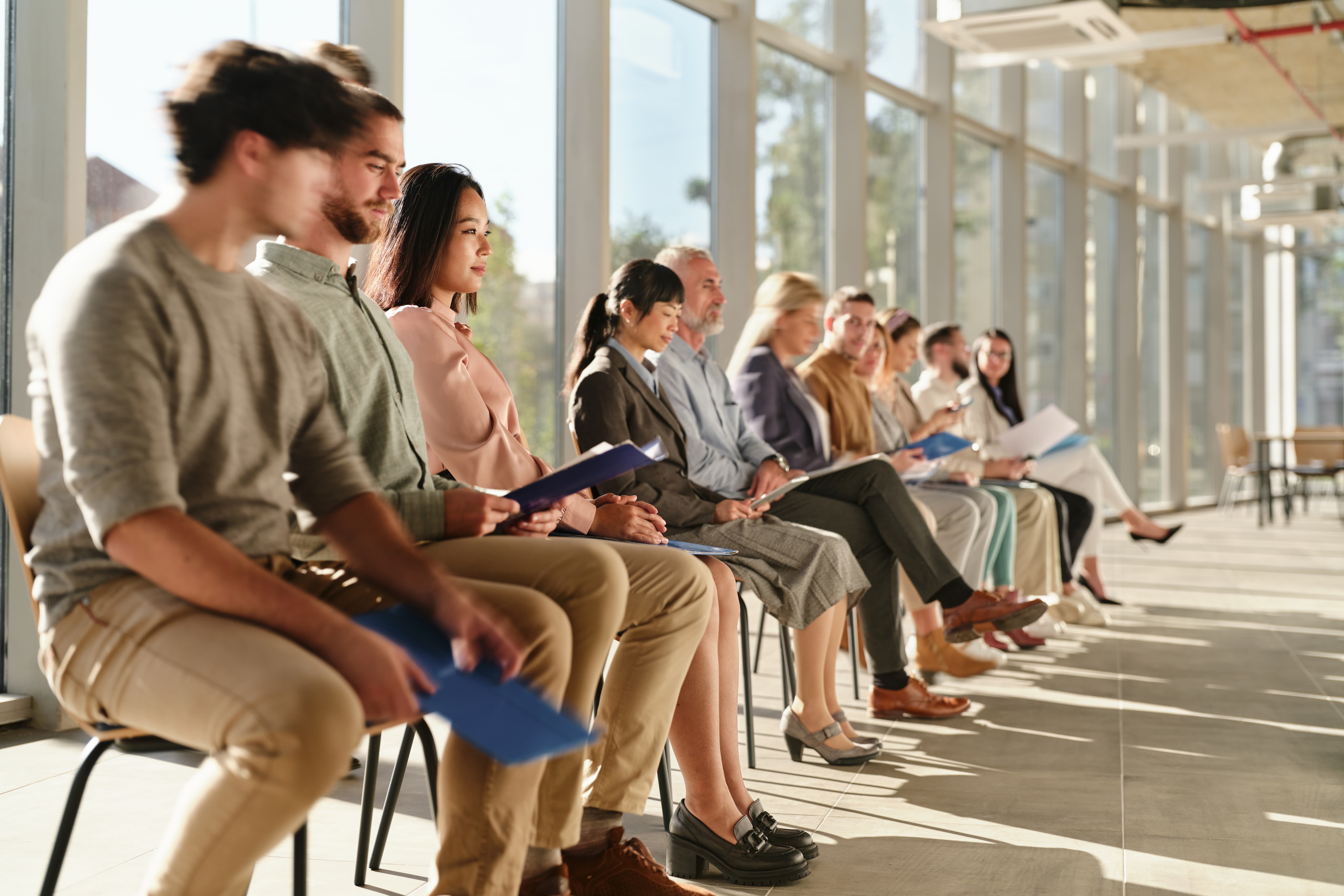 Group sitting in line holding folders at hiring event in office