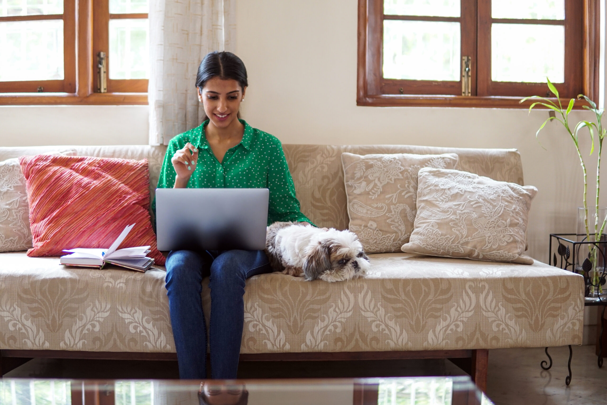 Person sitting on couch with a dog, working on a laptop.