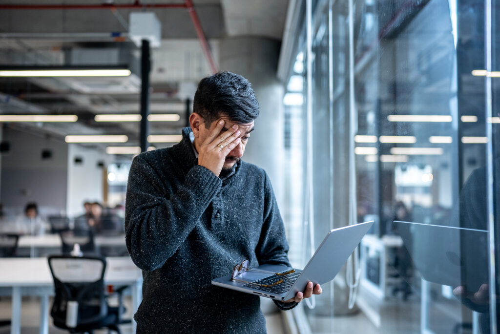 Person holding laptop in the office holding head looking worried