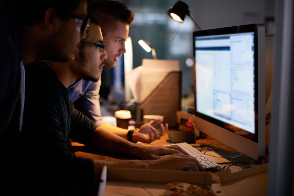 Coworkers gathered around a computer screen in a dimly lit office setting