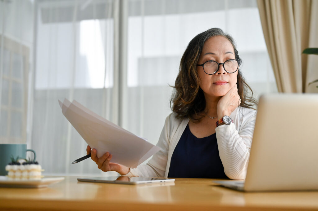 Person sitting at table looking at laptop and paperwork
