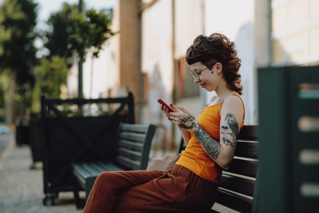 Young person sitting on bench looking at cell phone in an outside setting in a park