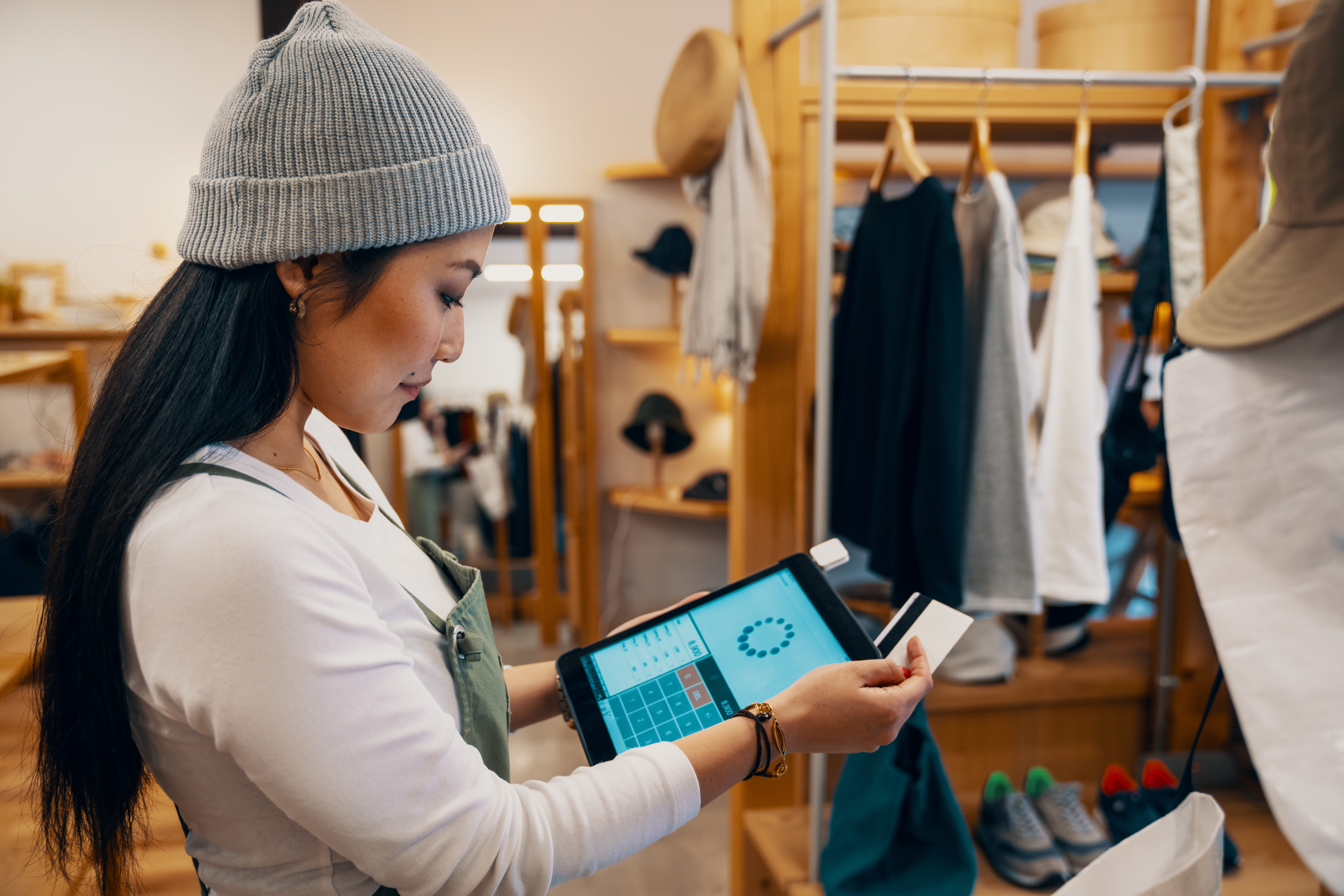 Retail shop clerk taking a mobile credit card payment on a digital tablet in a clothing boutique