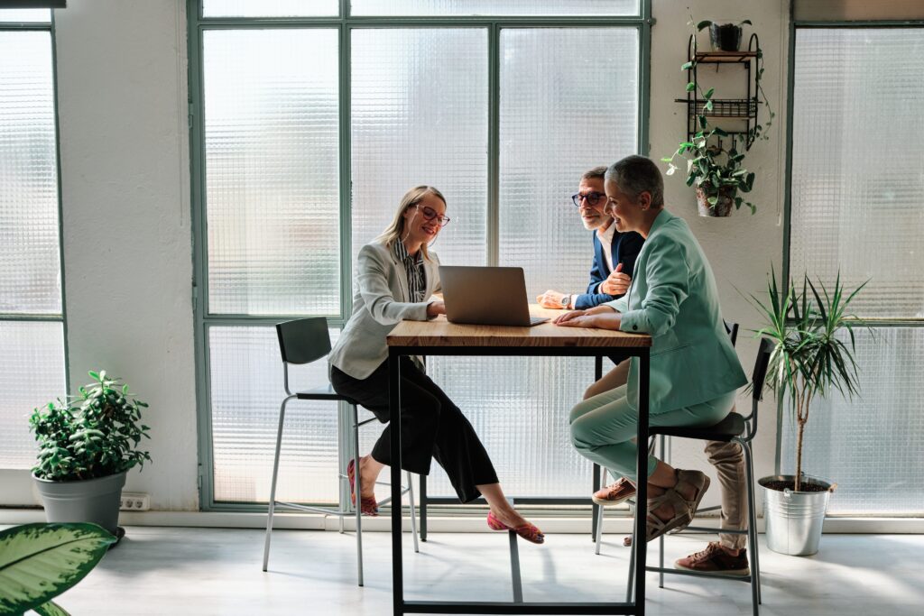 A financial advisor meeting with clients in the office with windows and plants behind them, one financial advisor and two clients at a table