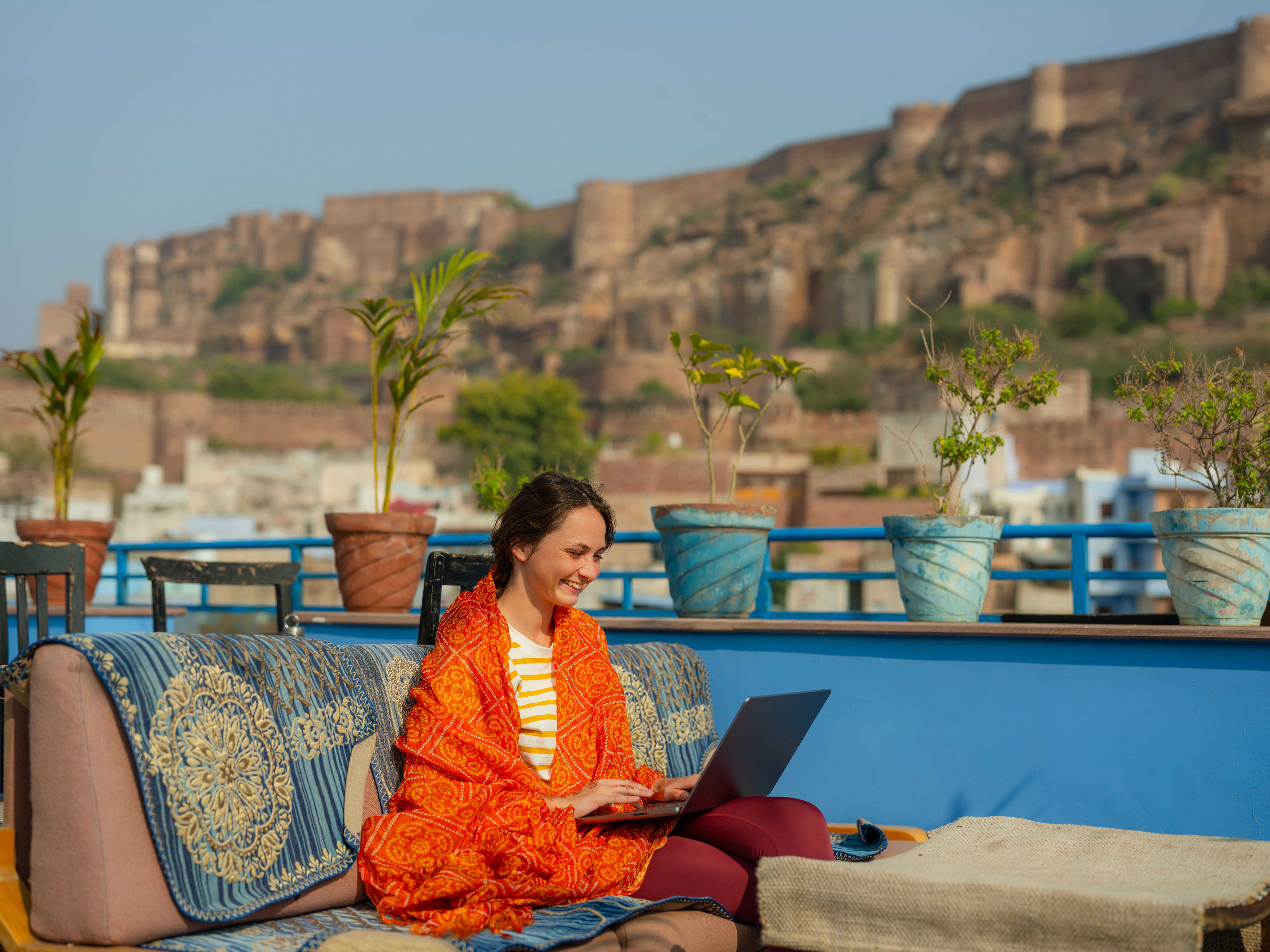 Person with laptop on balcony overlooking fort in Jodhpur blue city, India